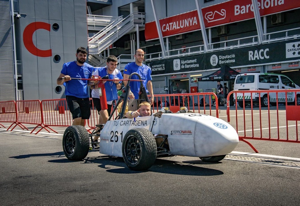 Tres integrantes del equipo empujan el monoplaza por el pit lane mientras el piloto hace un gesto de ánimo