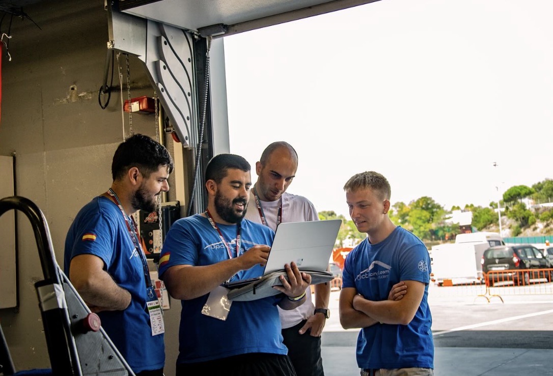 Tres integrantes del equipo mirando juntos un portátil a la entrada del box