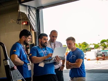 Cuatro integrantes del equipo mirando un portátil junto al box